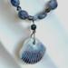 Closeup of blue sodalite beads and ceramic shell pendant. The pendant has blue and brown vertical ridges.